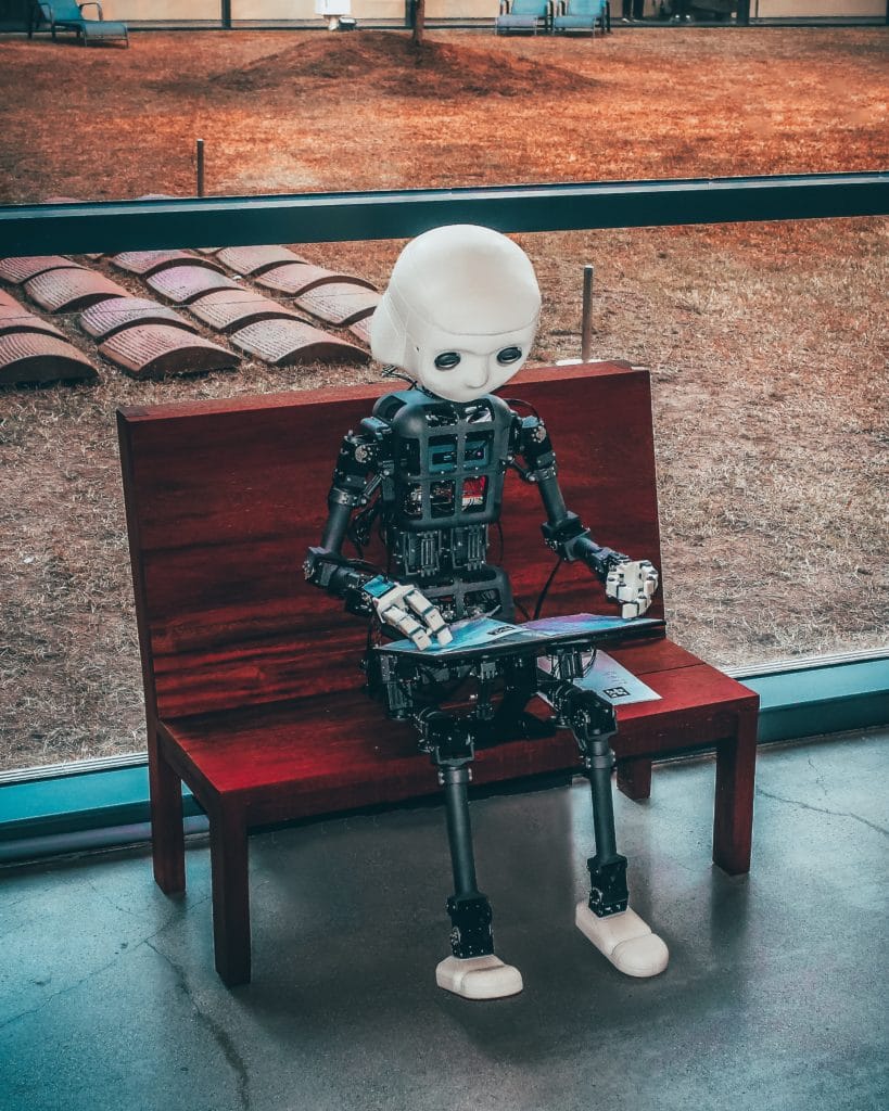 en robot sitter på en benk og blar i en bok