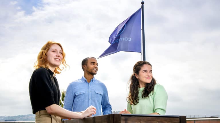 Tre ansatte på takterrassen ser utover forann flagget